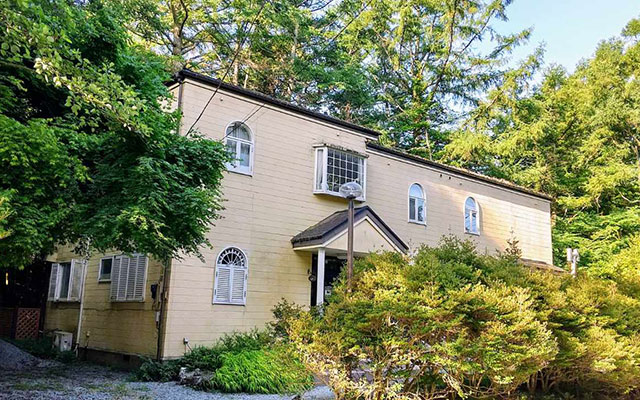 山梨県のプライベートハウスバイロン｜青空の下、広大な芝生のドッグランを元気に走る白い大型犬。背景には湖とコテージが見える。