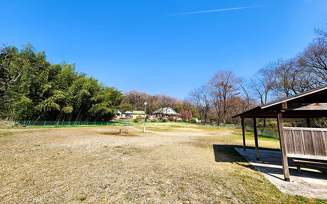 栃木県・那須の貸別荘『ハートヒルズ』にある、周囲を竹林と森に囲まれた広大な天然芝のドッグラン。青空の下、屋根付きの休憩スペースが併設されている。