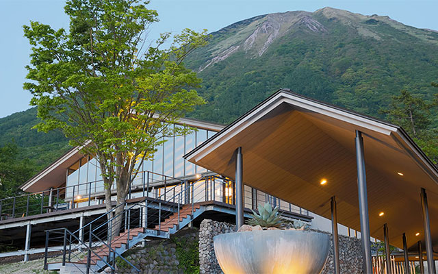 狗賓大山（ぐひんだいせん）｜鳥取県　大山の犬と泊まれる宿｜夕暮れ時、雄大な大山（だいせん）を背景にしたモダンな建築の宿泊施設。温かい照明が灯っている。