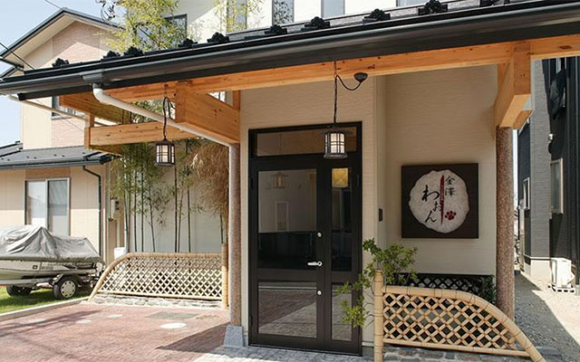 石川県にあるペットと泊まる宿「金澤わおん」の外観。和モダンな玄関口には木製の梁と伝統的な提灯型の照明があり、右側には肉球マークが入った「金澤わおん」の看板が掲げられています。