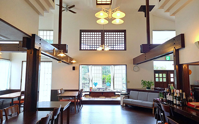 静岡県のクイール　～ペットと一緒に過ごす宿～｜高い吹き抜けと太い木の梁が印象的な、開放感あふれるペンションのダイニングルーム。奥の窓からは緑が見える。