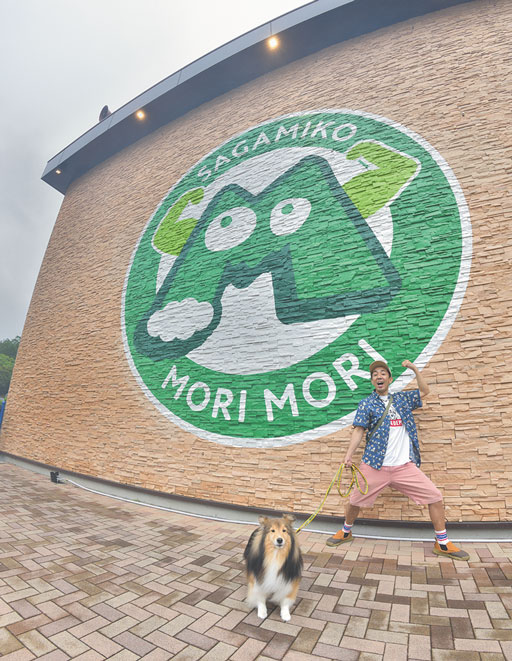 神奈川県相模原市の相模湖の近くにある「さがみ湖MORIMORI]の看板で記念撮影する松本さんとアンディ